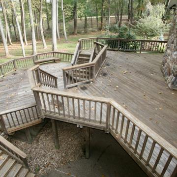 Weathered multi-level wooden deck with railings in wooded backyard