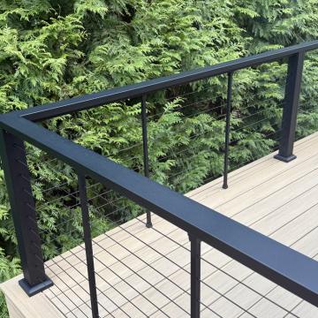 Black cable railing on composite deck beside evergreen privacy hedge