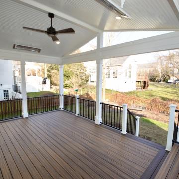 Covered open-air porch with composite decking, black railing, and ceiling fan