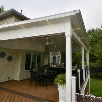 Covered open-air porch with white columns, deck seating, and railing