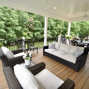 Covered open-air porch with wicker seating, dining area, and grill