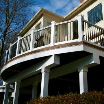 Curved elevated backyard deck with white railings and support posts