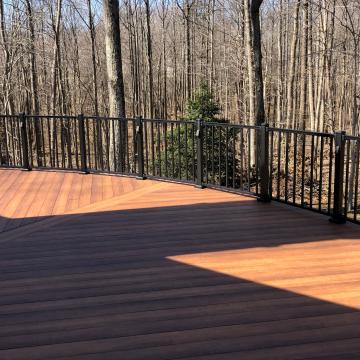 Curved wood deck with black railing overlooking leafless wooded yard