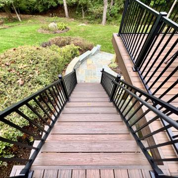 Deck stairs with black railings leading to a stone patio