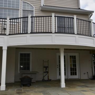 Elevated curved deck with black railing above covered stone patio