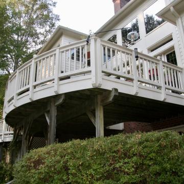 Elevated curved white deck attached to brick and siding home