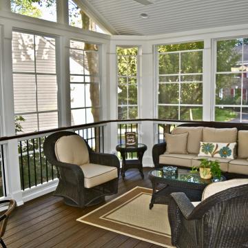 Enclosed porch with wicker seating, large windows, and wood-look flooring
