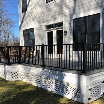 Gray backyard deck with black railing and white lattice skirting
