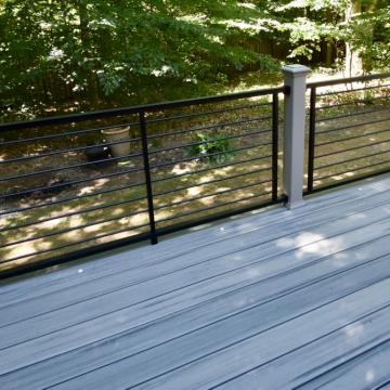 Gray composite deck with black cable railing overlooking wooded backyard