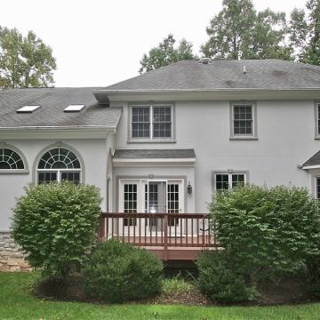Rear exterior of stucco house with deck and large arched windows