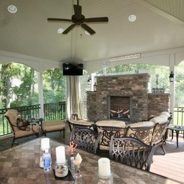 Screen porch with stone fireplace, ceiling fan, and cushioned seating