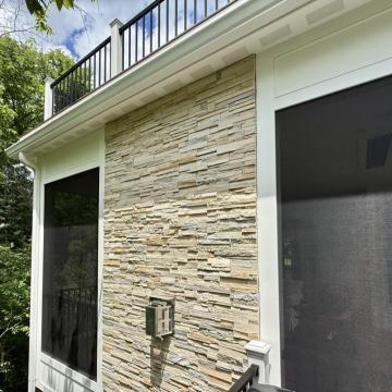 Screened porch exterior with stacked stone wall and upper deck railing