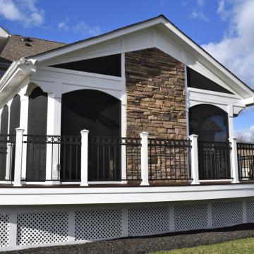 Large screened porch with stone chimney and wraparound deck railing