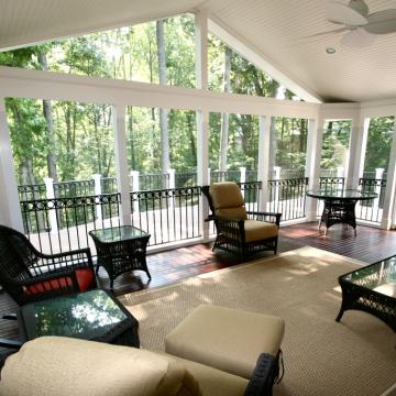 Spacious screened porch with vaulted ceiling, wicker seating, and wooded views