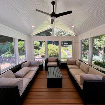 Bright screened porch with wicker seating, wood floor, and ceiling fan