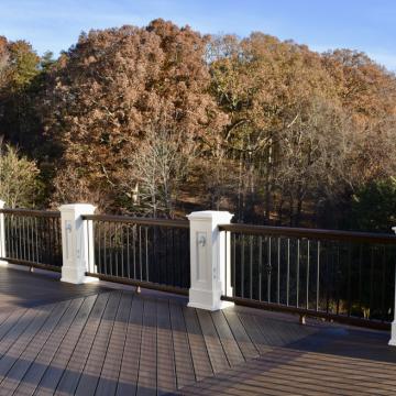 Spacious deck with white posts overlooking wooded backyard in autumn