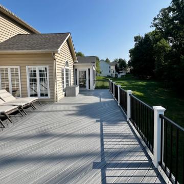 Spacious gray composite deck with black railing beside backyard lawn