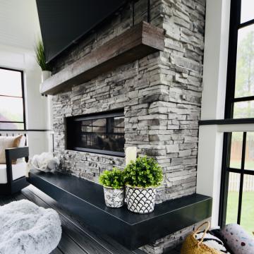 Stone fireplace with wood mantel in a bright screened porch