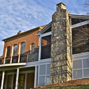 Tall stone outdoor fireplace beside a screened patio addition