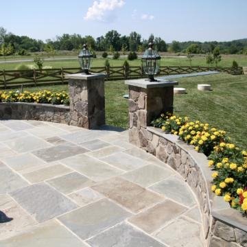 Stone patio with curved flower beds and lantern-topped pillars