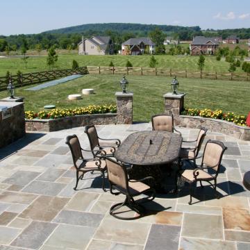 Stone patio with dining set, grill, and low stone walls
