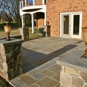 Stone patio with low wall and capped columns by brick home