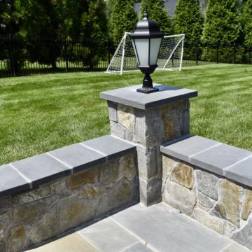 Stone patio wall with lantern post beside a lawn