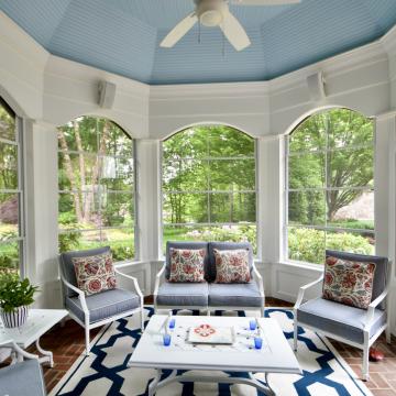 Bright sunroom with arched windows, blue ceiling, and cushioned seating
