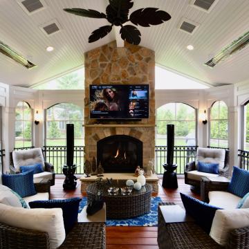 Three season room with stone fireplace, TV, and wicker seating
