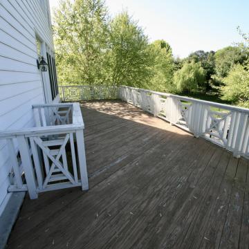 Weathered upper deck with white railing overlooking mature trees