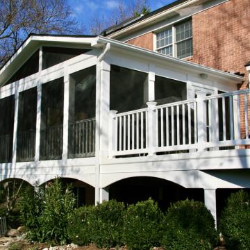 White elevated screen porch attached to brick home with deck railing