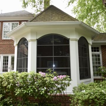White screened porch addition with arched openings beside brick home