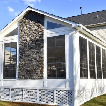 White screened porch with tall stone chimney and gabled roof