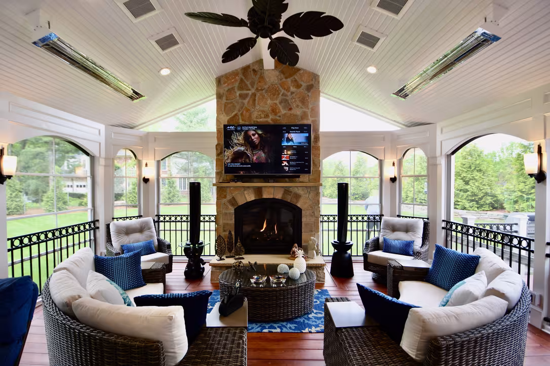 Three season room with stone fireplace, TV, and wicker seating